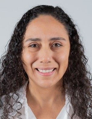 Smiling woman with curly dark hair against a light gray background