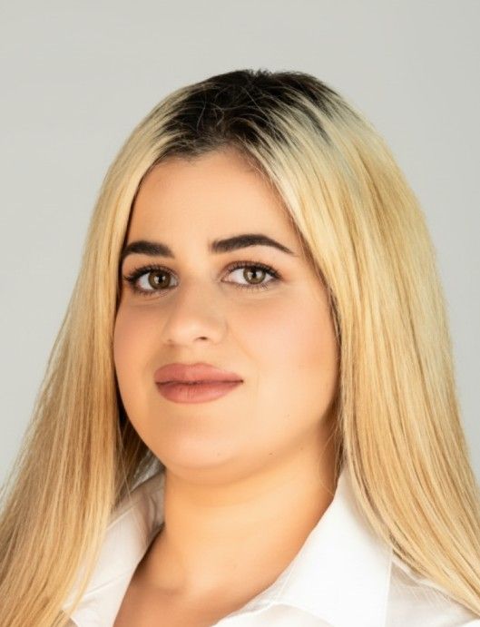 Portrait of a person with long blonde hair, wearing a white shirt, against a light background