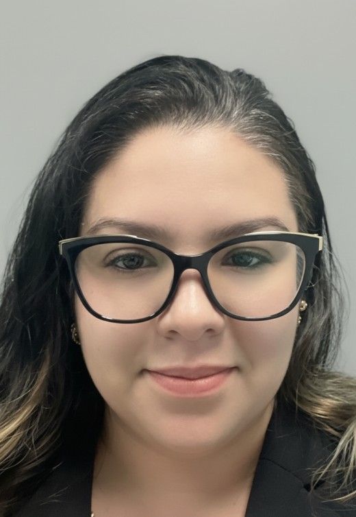 Headshot of a person wearing black glasses, smiling slightly against a plain gray background