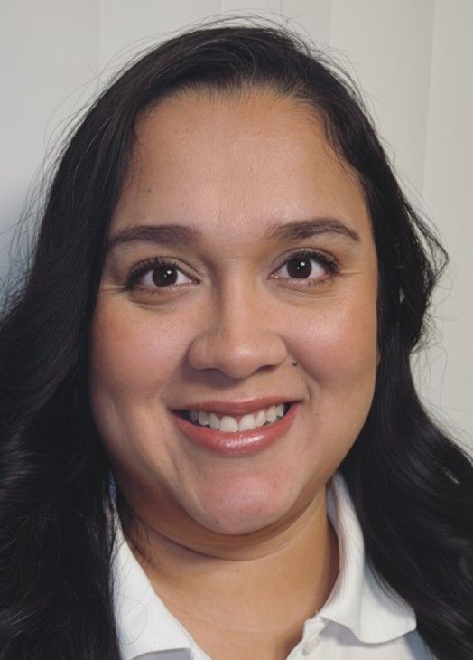 Portrait of a smiling person with dark hair, wearing a white collared shirt and gray blazer.