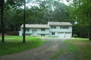 White two-story house with garage on a tree-lined driveway in a grassy yard
