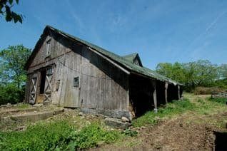 Old weathered wooden barn on a grassy field under a clear blue sky.