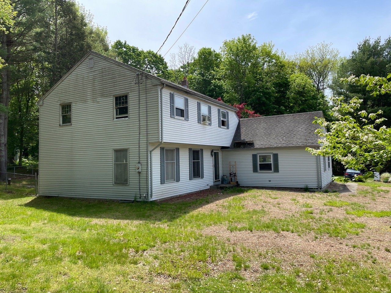 Two-story gray house with white trim and an attached wing, surrounded by trees and a grassy yard