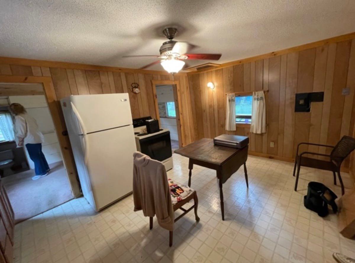 Wood-paneled kitchen with white appliances, tiled floor, table, chairs, and a person by the doorway