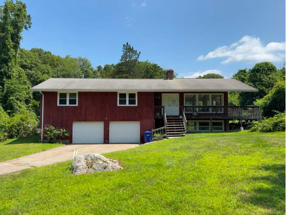 Red house with two-car garage and front porch on a grassy lawn under a blue sky