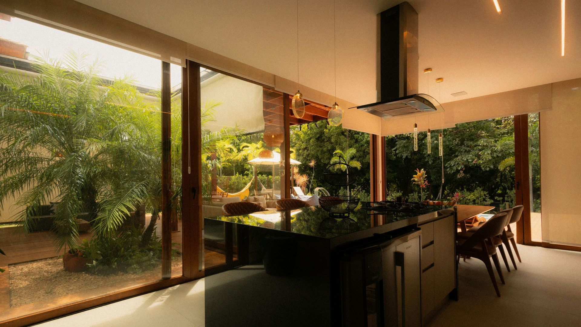 Modern kitchen overlooking a lush tropical patio through large glass doors, with warm evening light