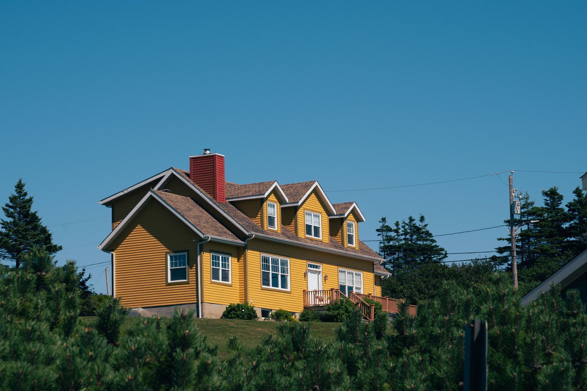 Yellow house with a red chimney on a hillside, surrounded by trees under a clear blue sky