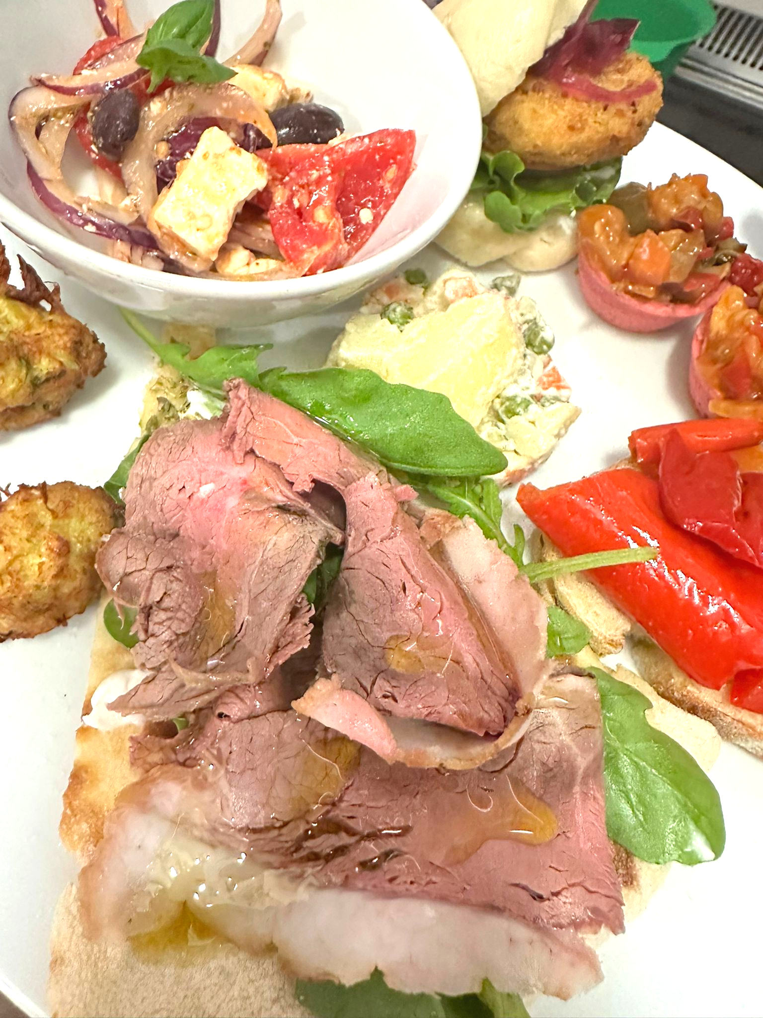Piatto di antipasti assortiti, tra cui carne, insalata e piccoli panini.
