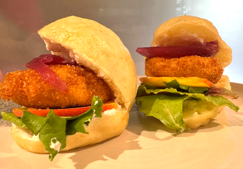 Due mini panini di pollo fritto con lattuga, pomodoro e cipolla sottaceto su un piatto bianco.