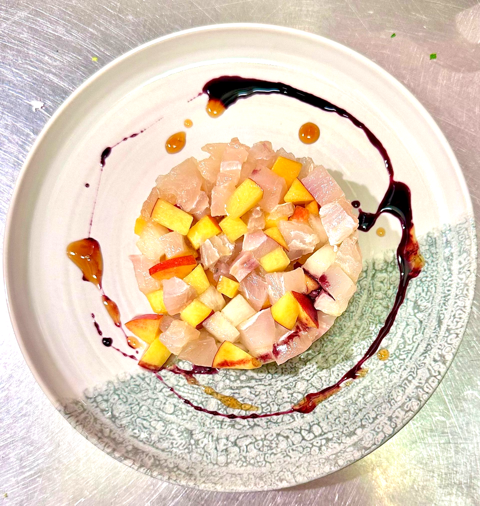 Macedonia di frutta rotonda con fette di pera, mango e puntini di salsa su un piatto.