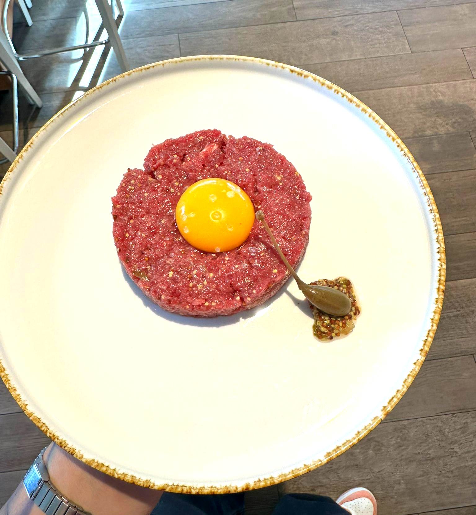 Tartare di manzo cruda con tuorlo d'uovo e senape su un piatto bianco.
