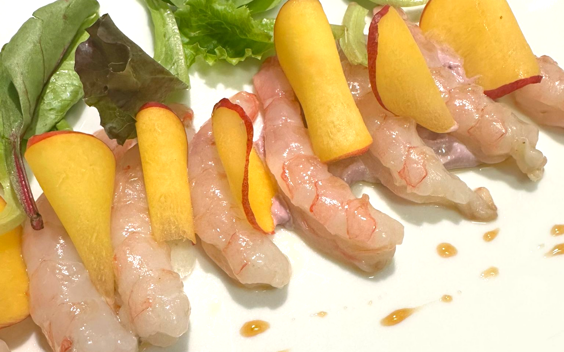 Raw shrimp dish with peach slices and greens, drizzled with sauce.