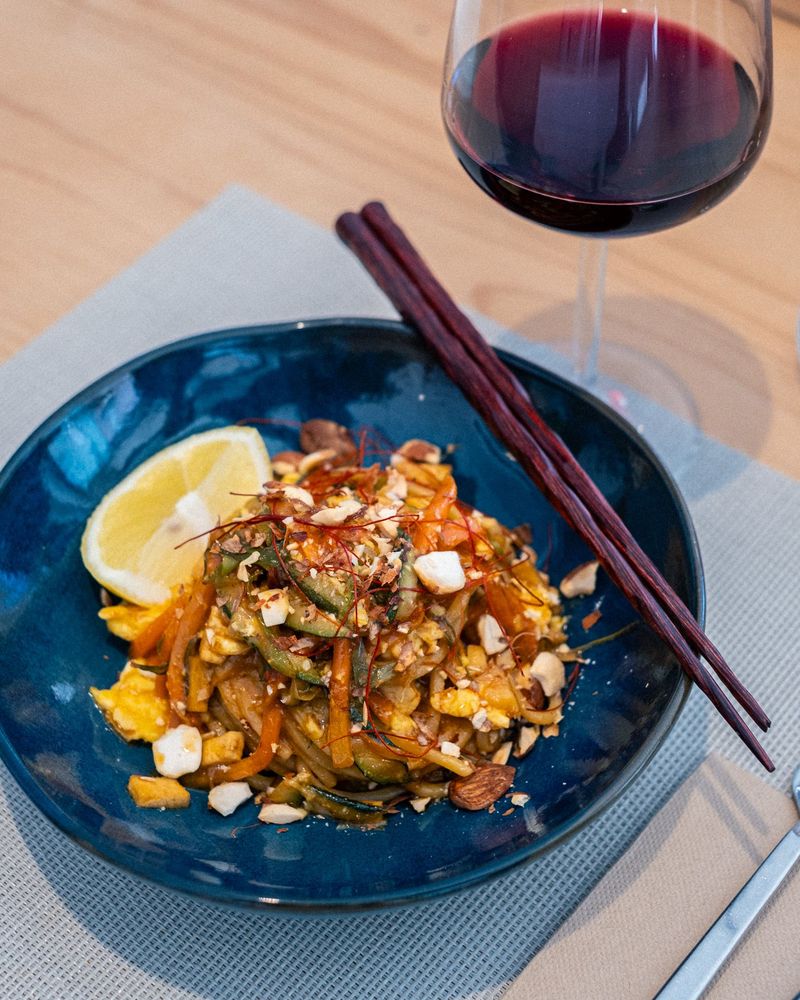 Pad Thai in ciotola blu, bacchette, bicchiere di vino rosso, fetta di limone.