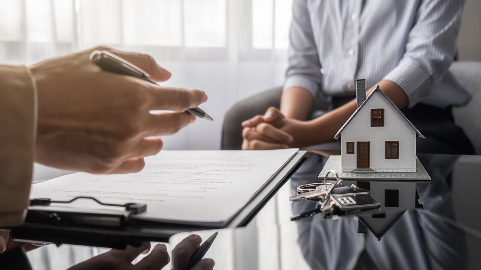 Hands signing a real estate contract beside a small house model on a desk
