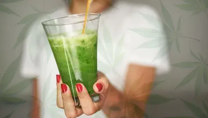Close-up of a green THC drink held by a person with red nail polish on. 