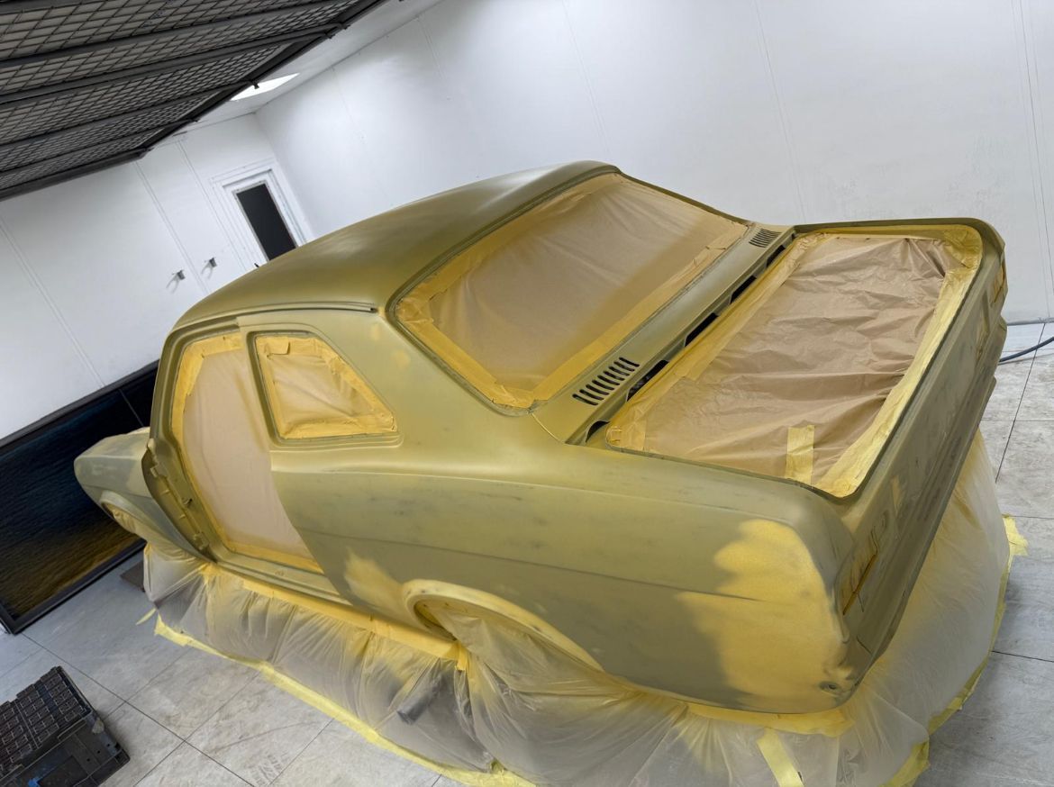 Gold-colored car body in a paint booth, covered with masking paper and tape