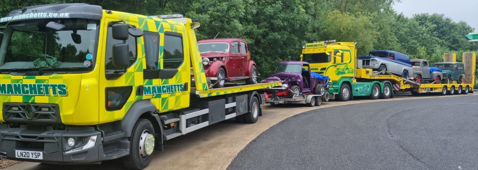 Bright yellow Manchetts tow trucks lined up on a curved road, carrying a red car and other vehicles.