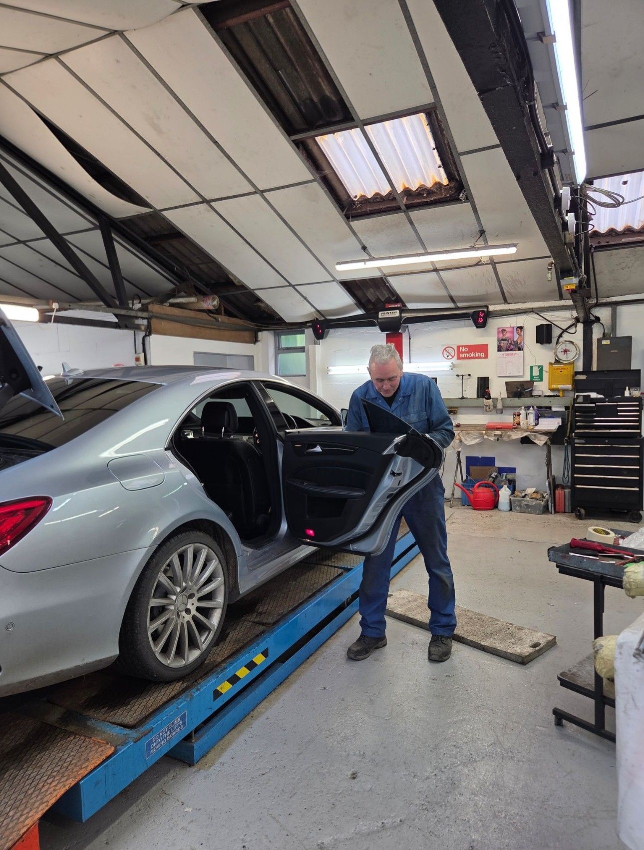 Mechanic working on a silver sedan in an auto repair shop on a lift
