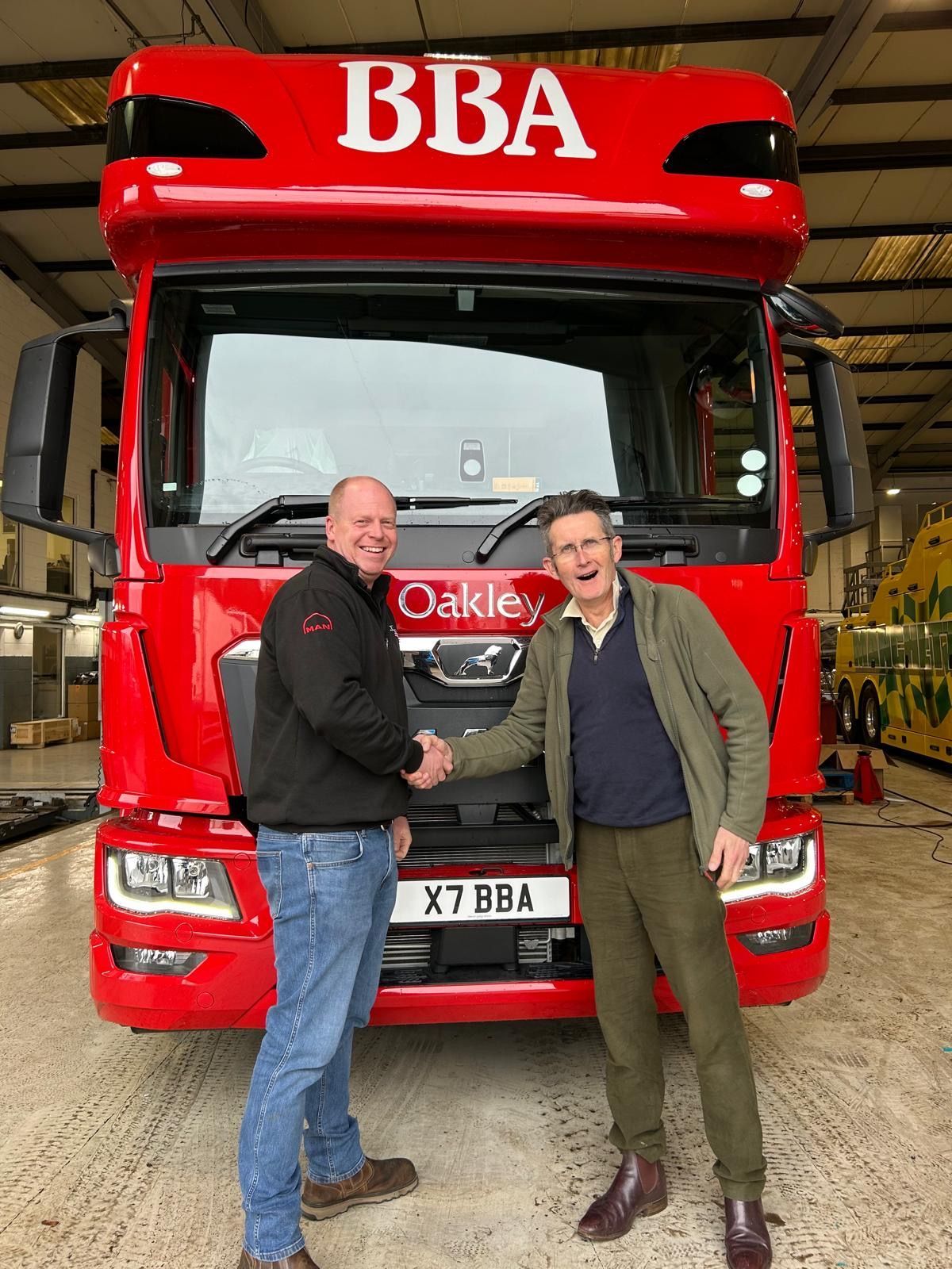 Two people standing in front of a red BBA truck in a warehouse, shaking hands.