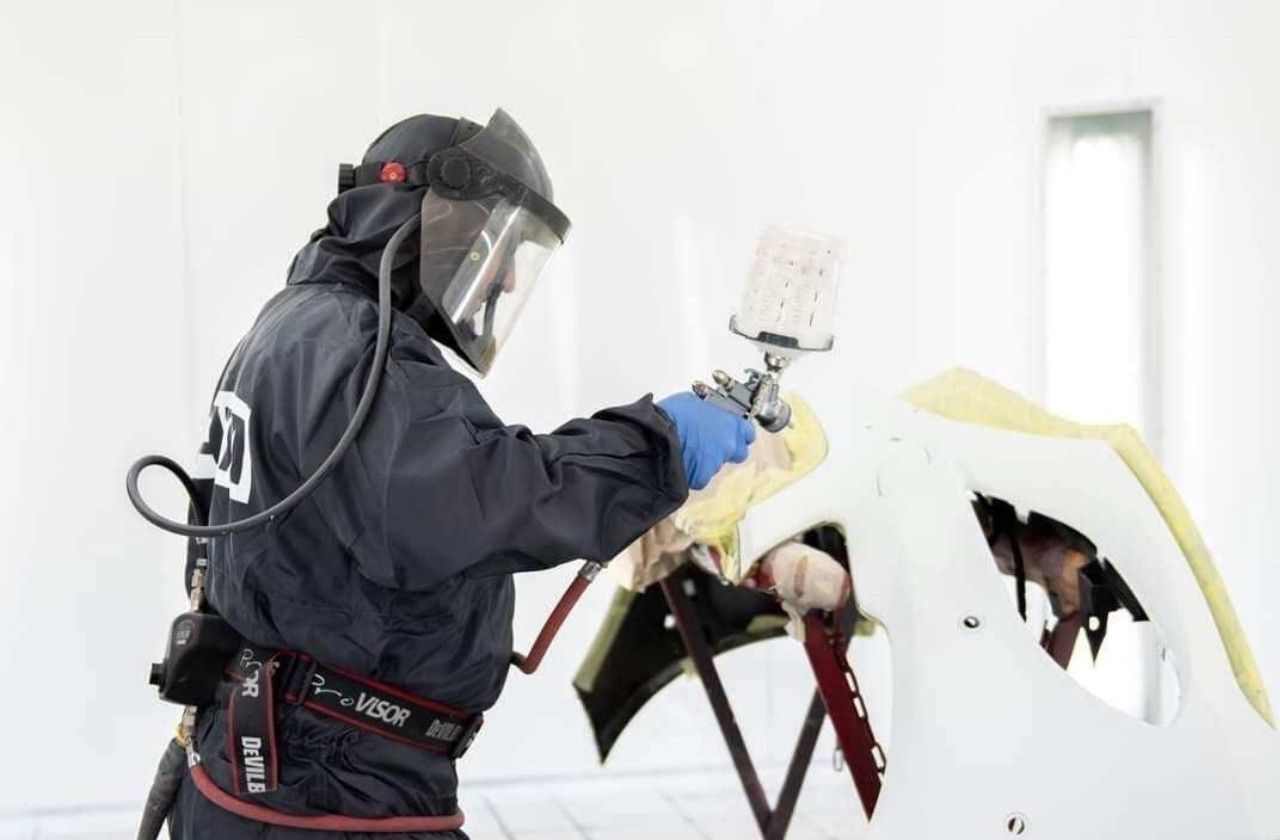 Worker in protective gear spray-painting a car body in a white auto workshop