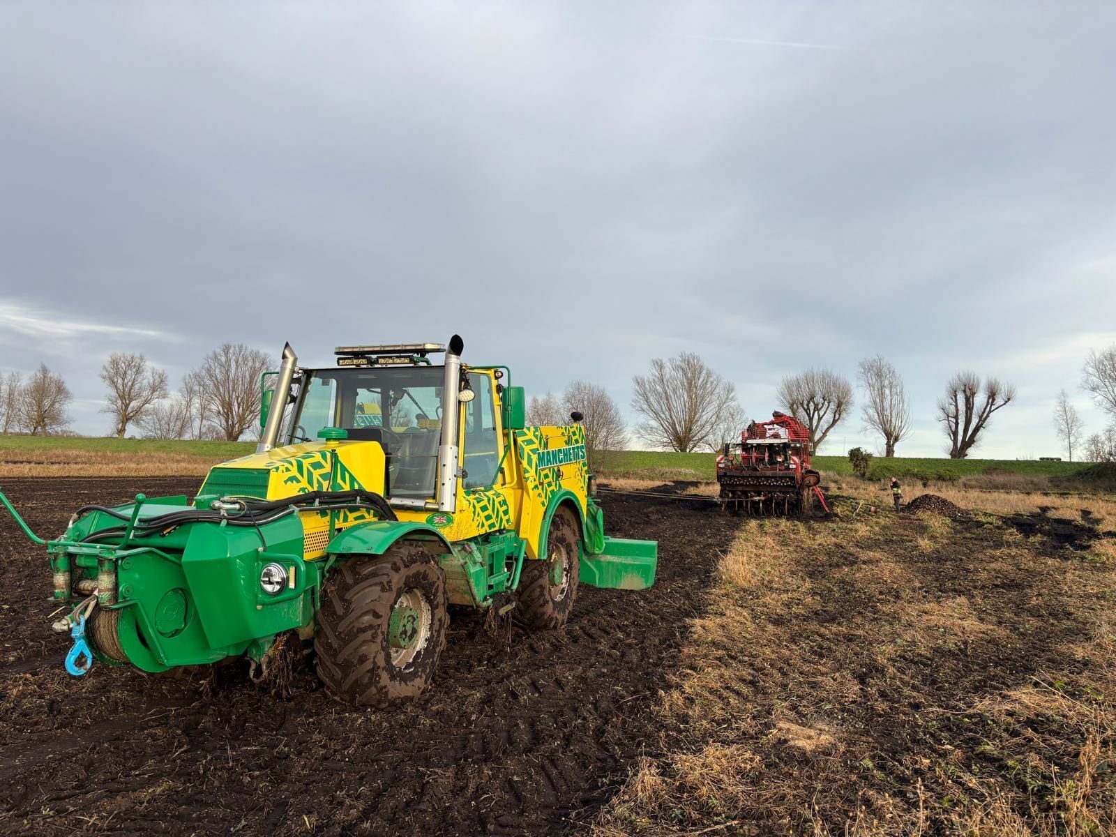 Manchetts Green and yellow tractor working a muddy field, with a second tractor in the background under a cloudy sky
