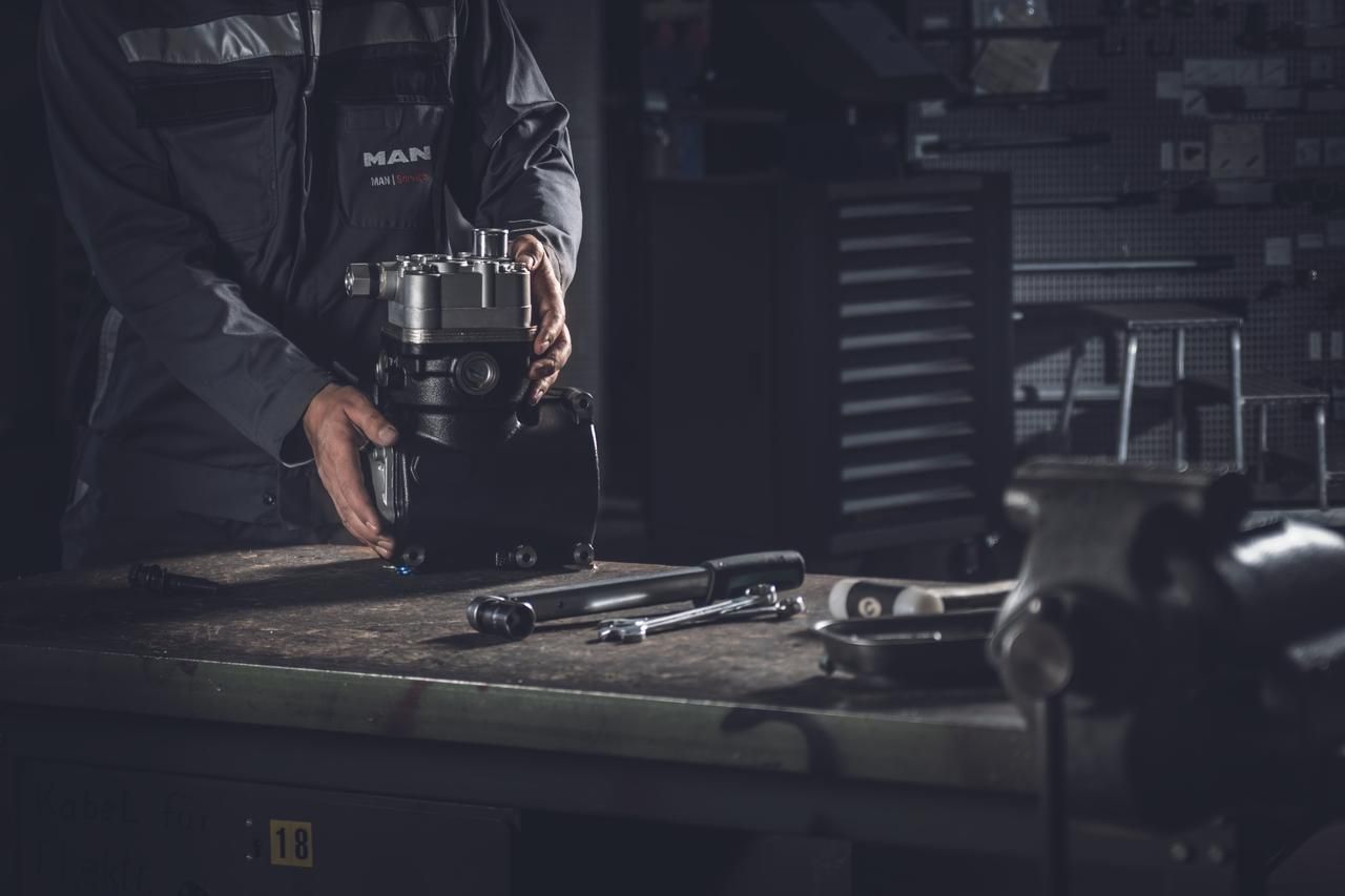 Worker sharpening a tool on a bench in a dim workshop, with other tools spread out nearby