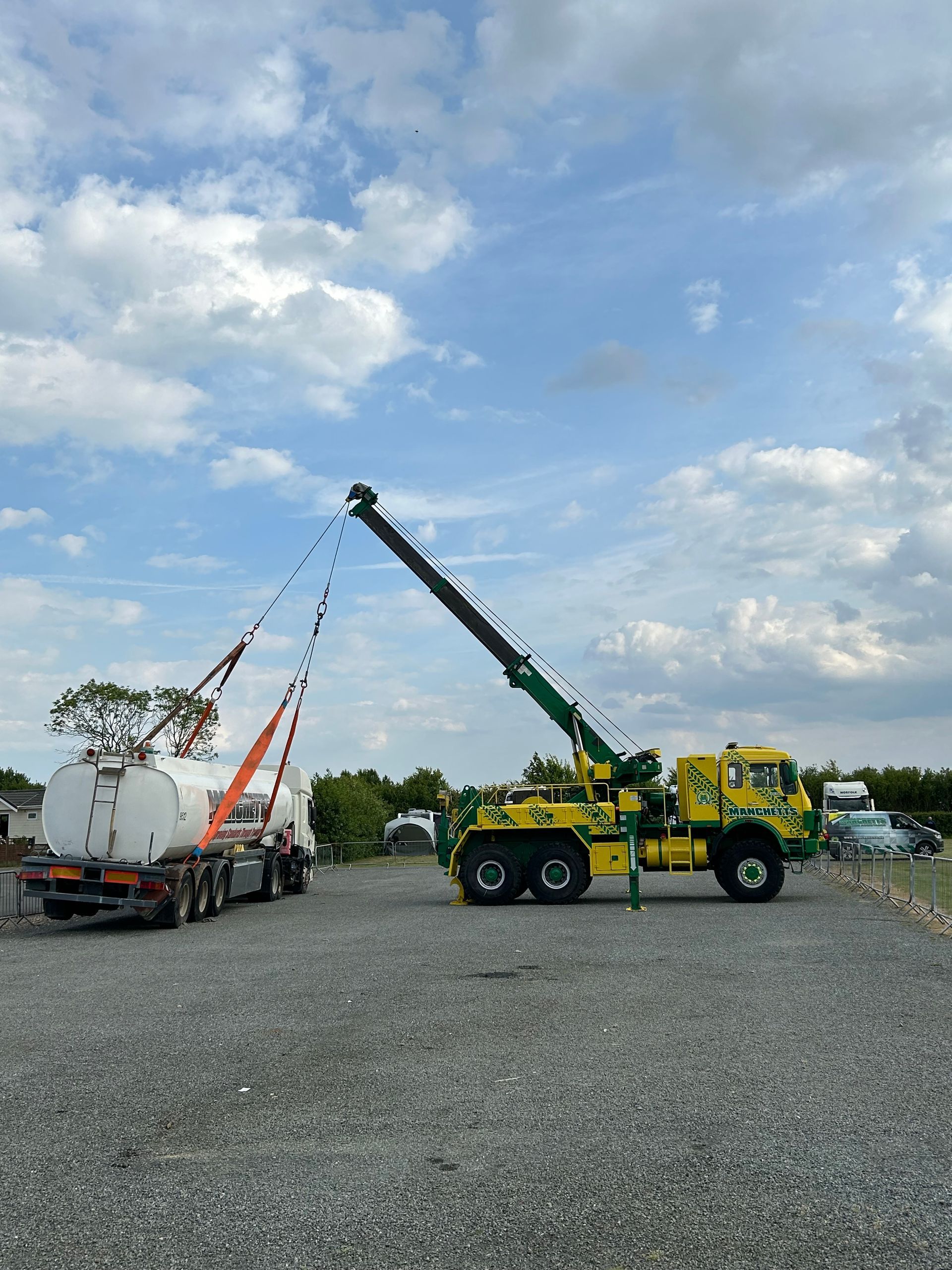 Yellow crane lifting a white truck in a gravel lot under a cloudy sky