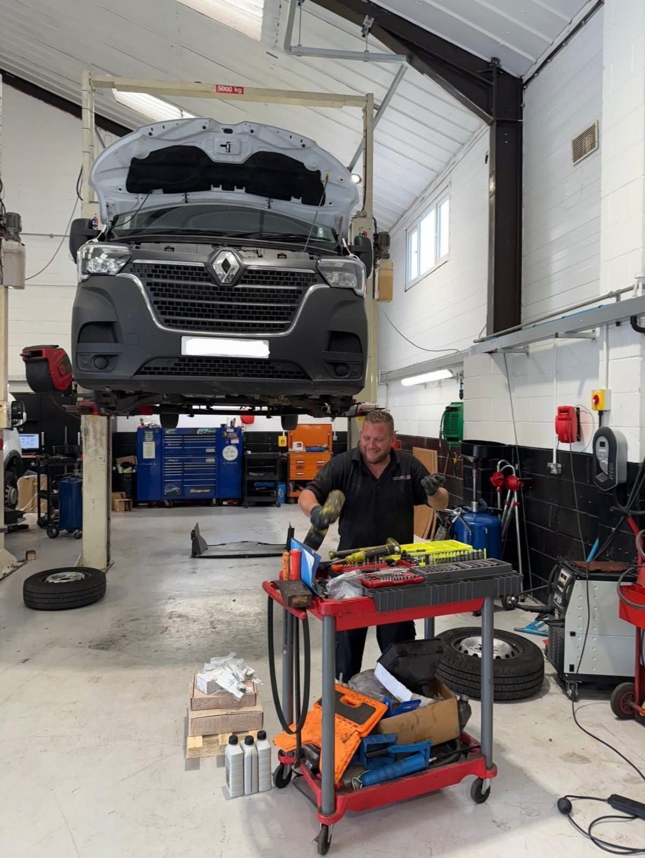 Mechanic working beneath a raised gray van in a bright auto repair bay