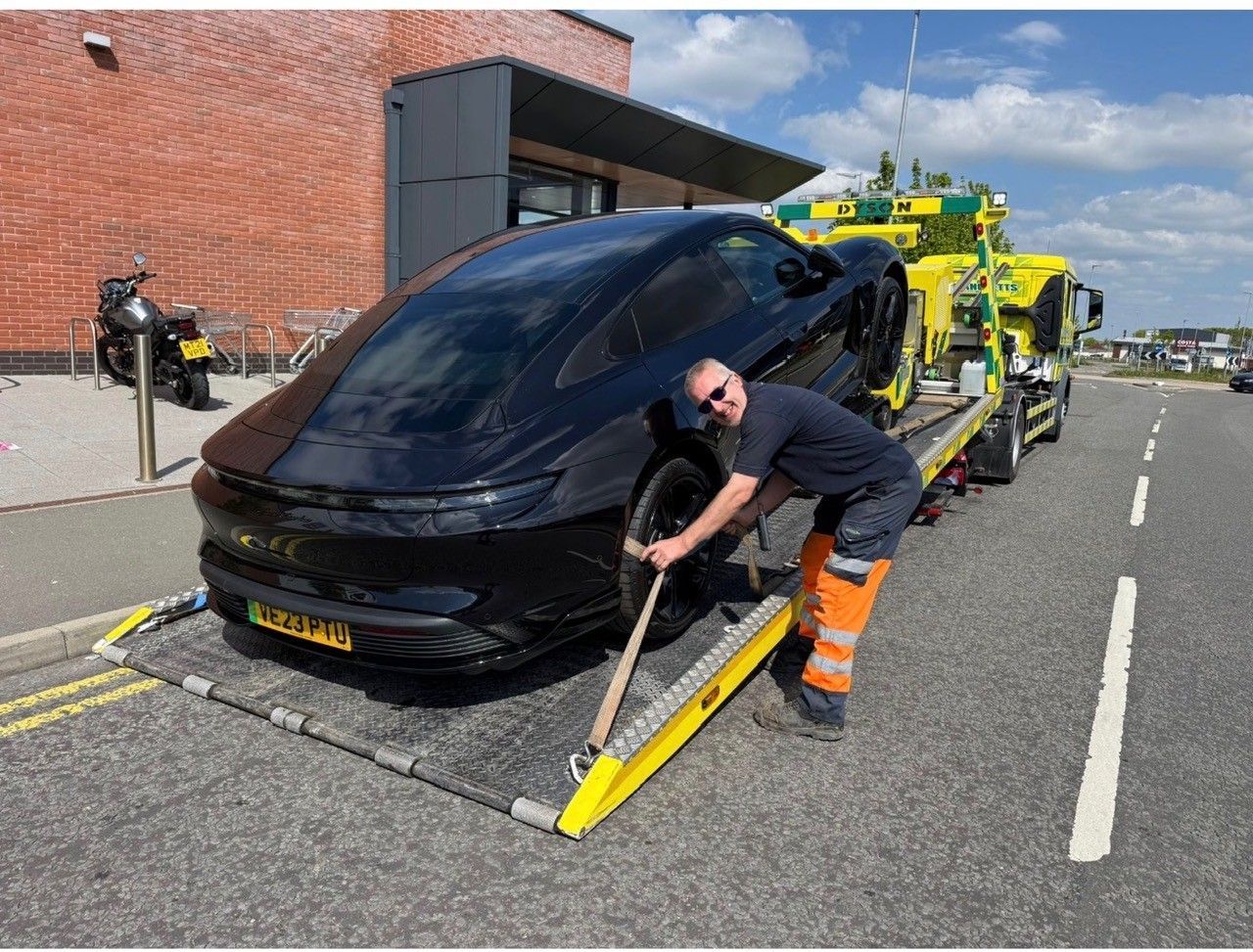 Worker loading a black car onto a Manchetts tow truck with a yellow ramp on a street