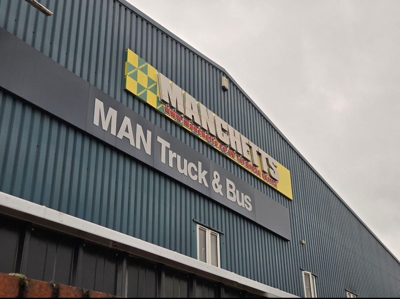 Manchetts Truck & Bus sign on a blue industrial building under an overcast sky