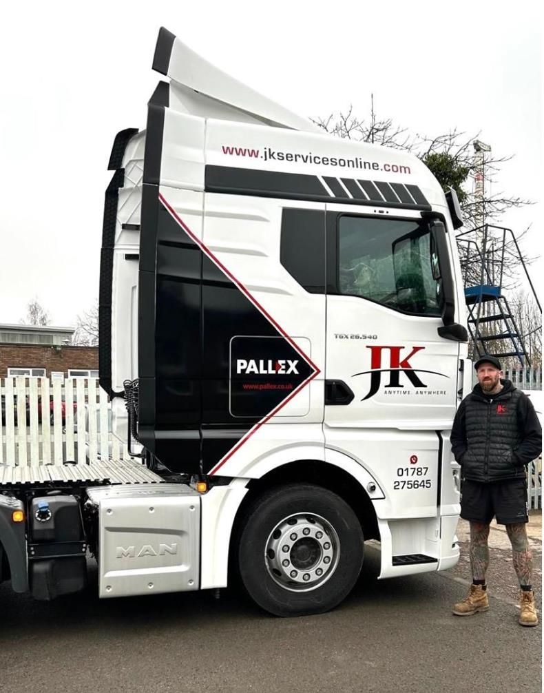 White semi-truck with black accents parked outdoors beside a man in a jacket.