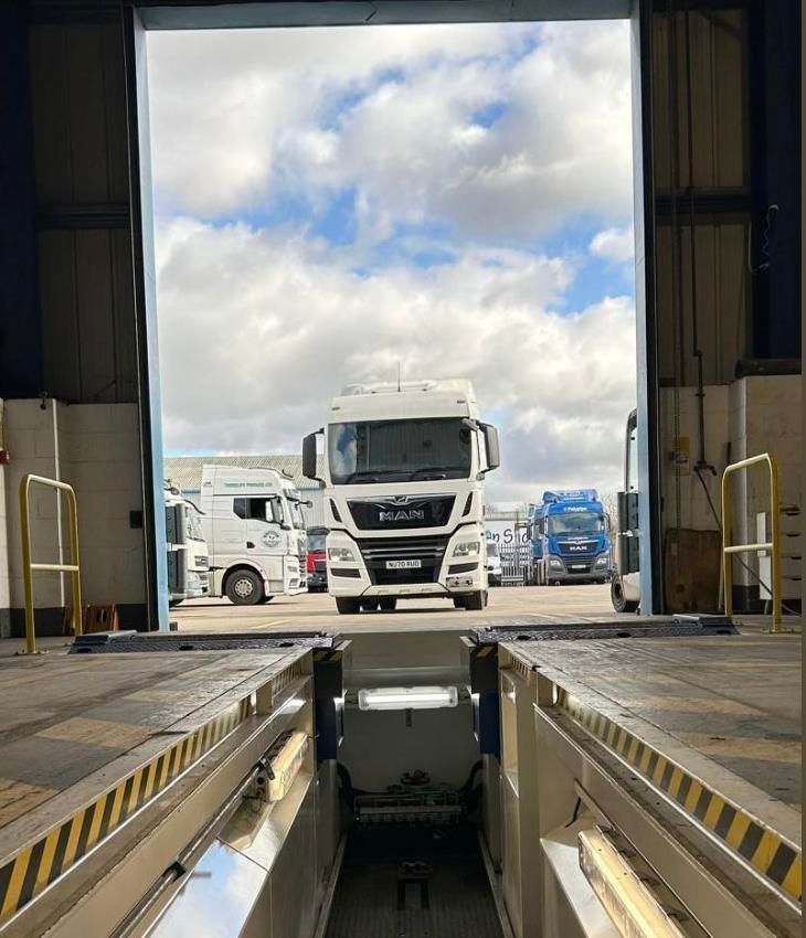 Truck loading bay with a white MAN truck outside under cloudy sky, viewed from a warehouse dock.