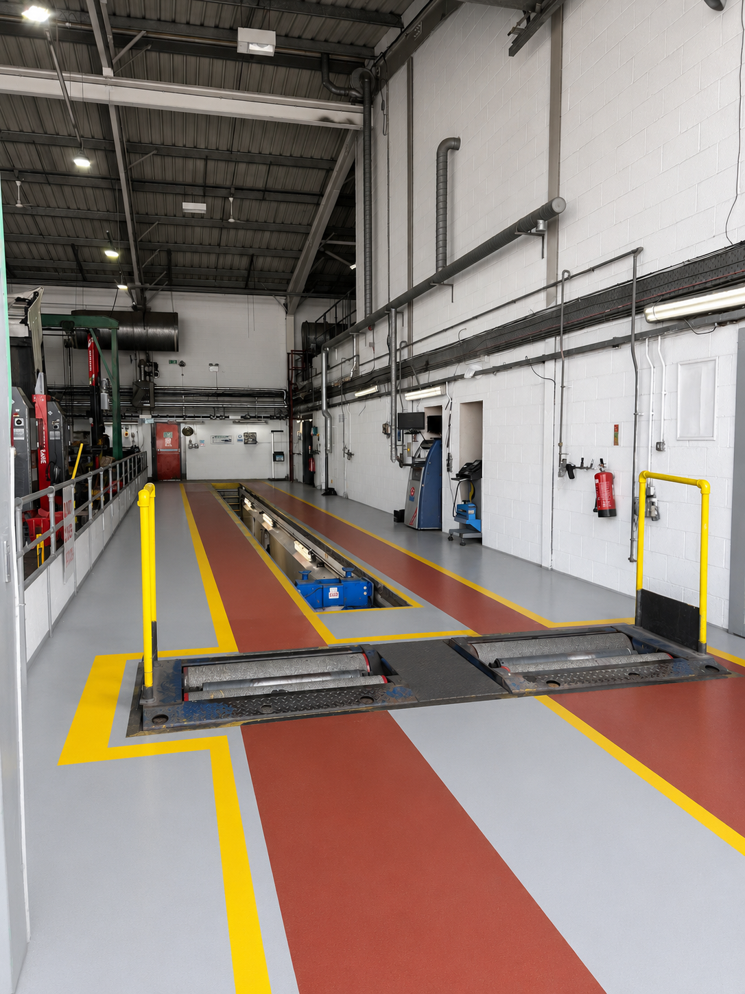 Industrial garage with yellow-marked floor lanes, a vehicle lift, and equipment along the walls.