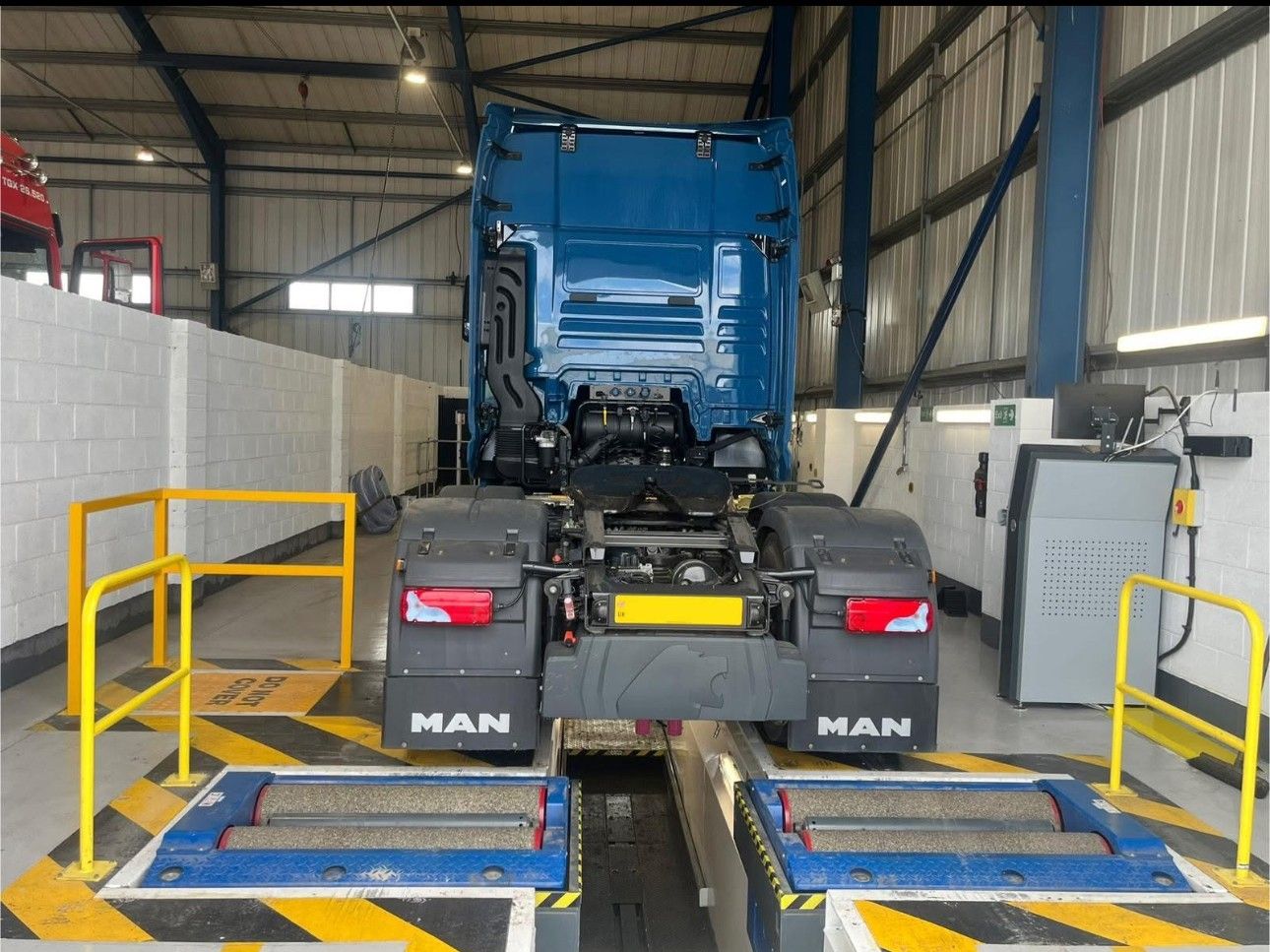 Blue MAN truck in an indoor service bay on raised inspection platforms, with yellow safety railings.