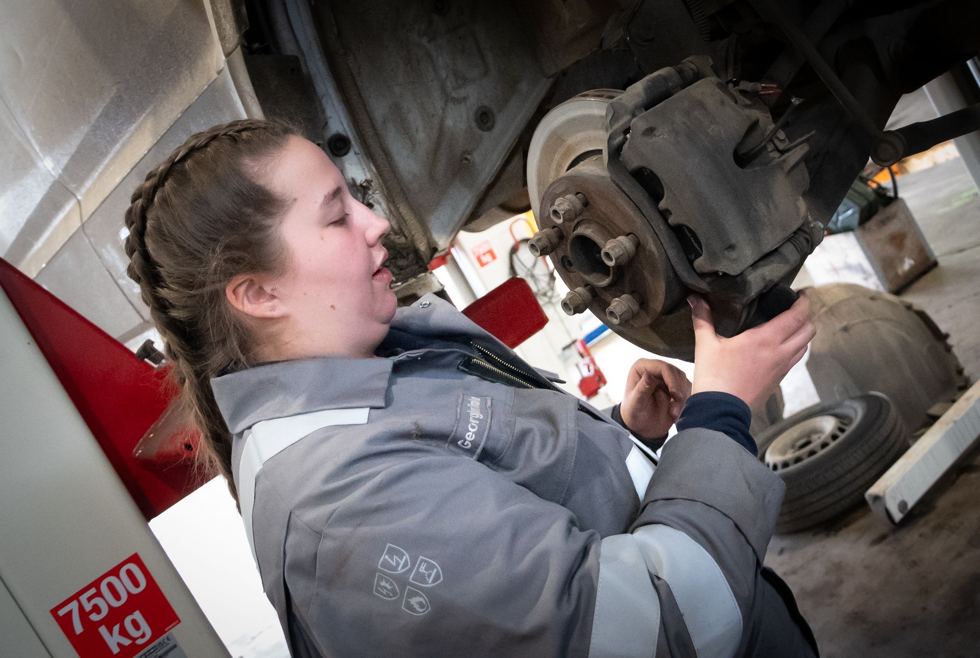 Mechanic inspecting a vehicle brake assembly under a raised truck in a garage