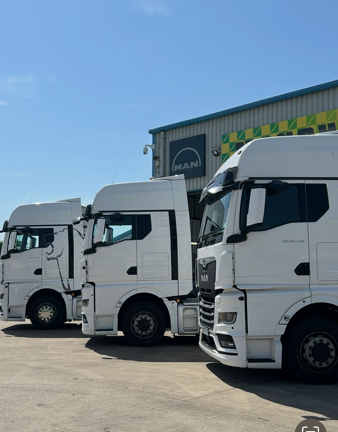 Three white semi-trucks parked outside a warehouse under a clear blue sky