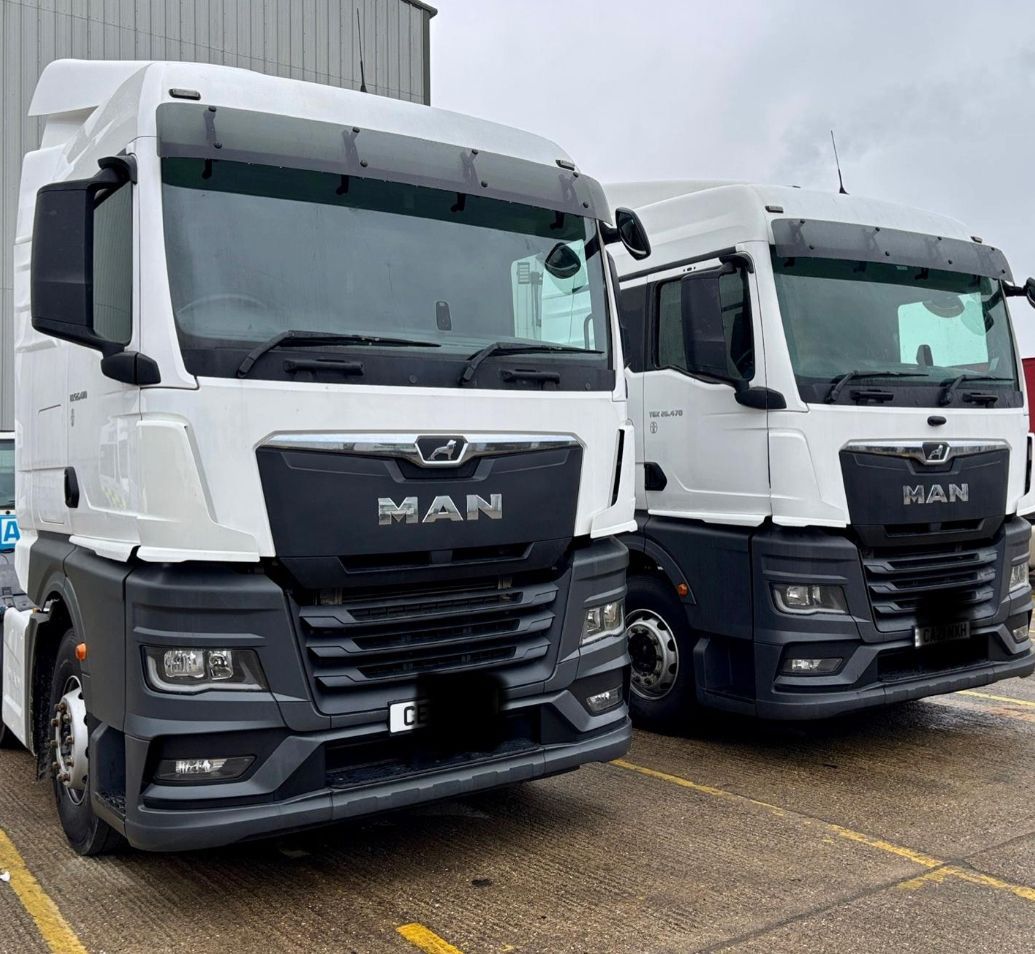 Two white MAN trucks parked side by side on a wet lot.