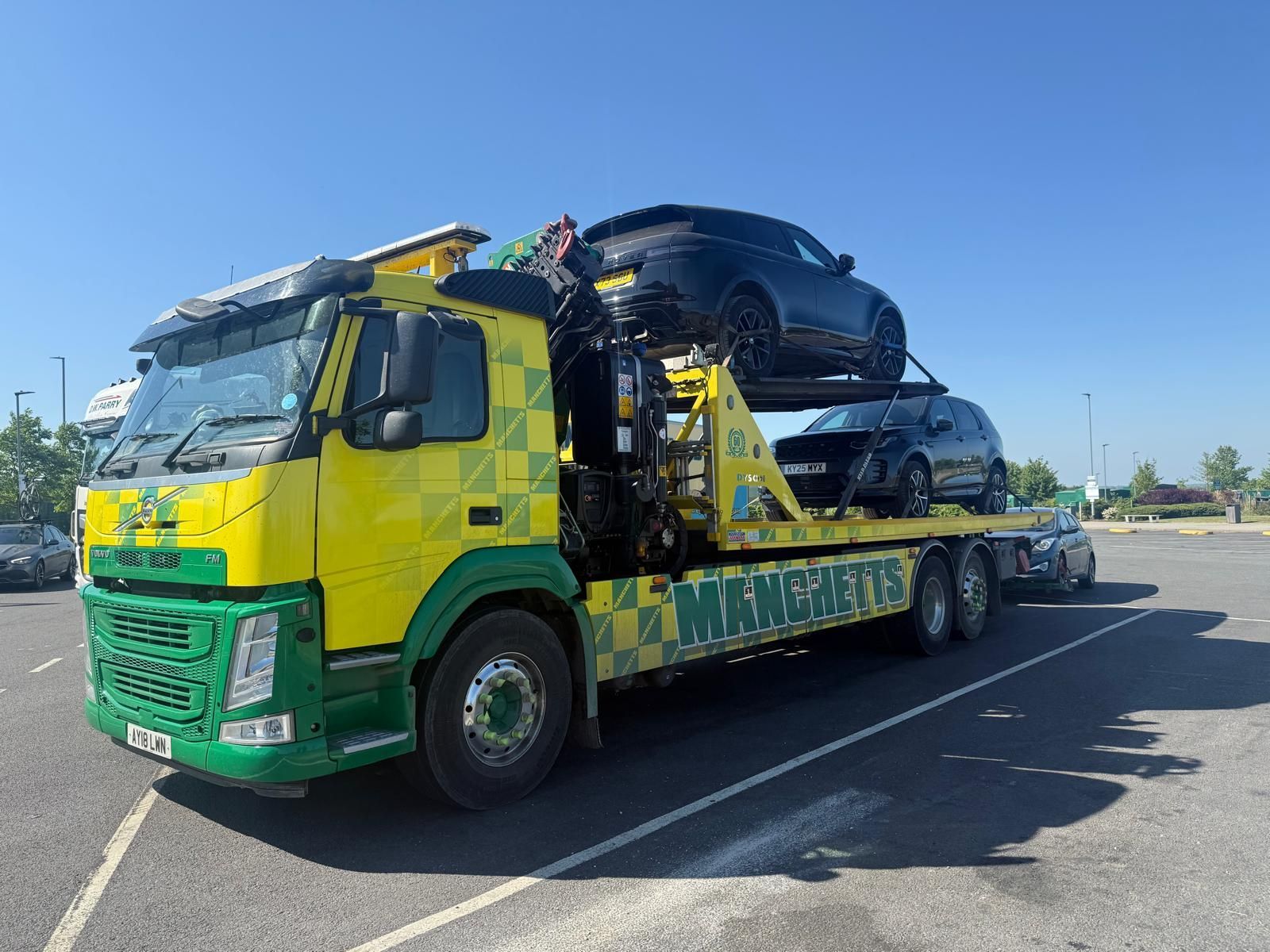 Yellow car carrier truck transporting black SUVs on a sunny road