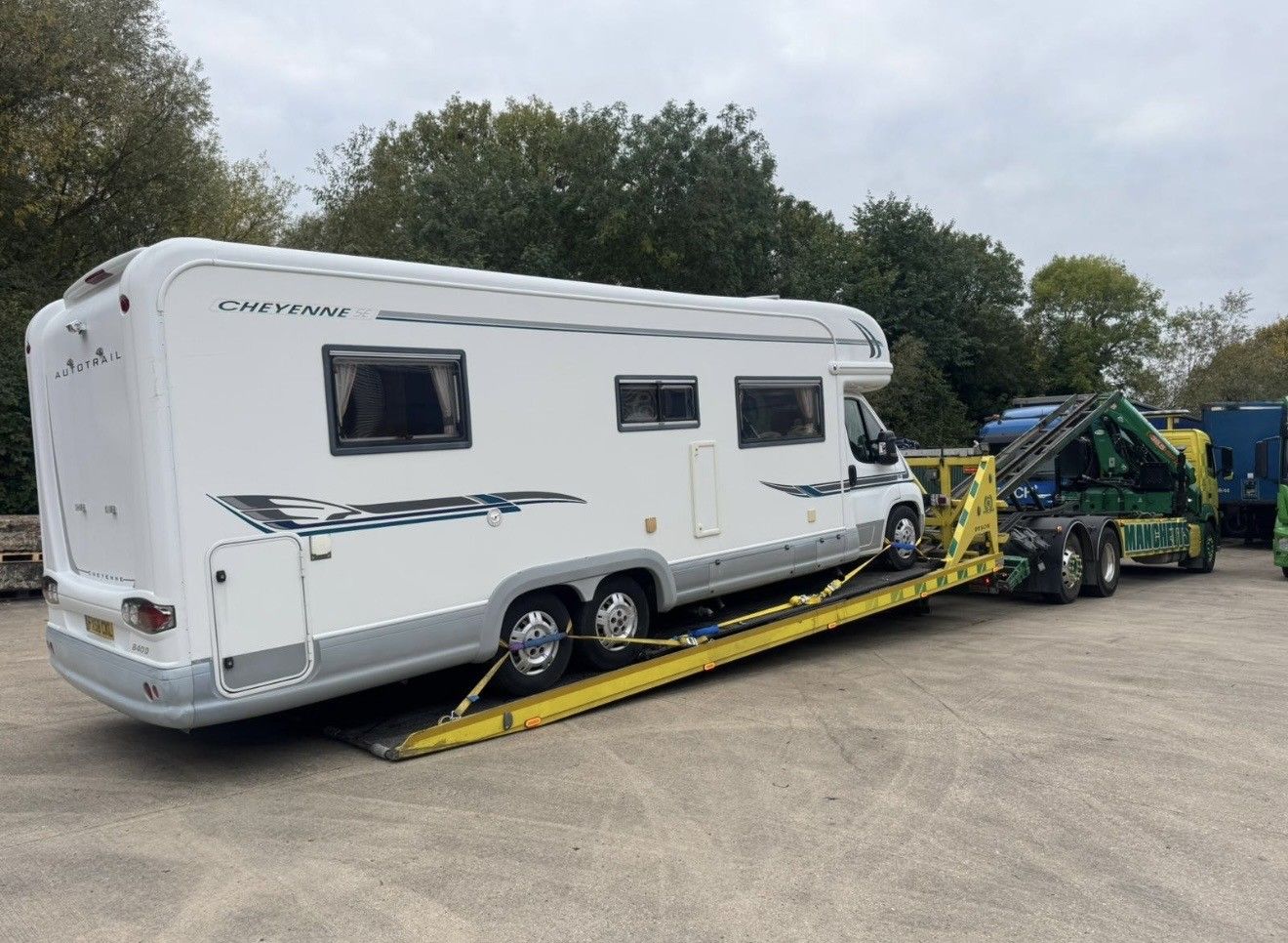 White caravan on a yellow tow dolly being pulled by a green towing vehicle on a roadside.