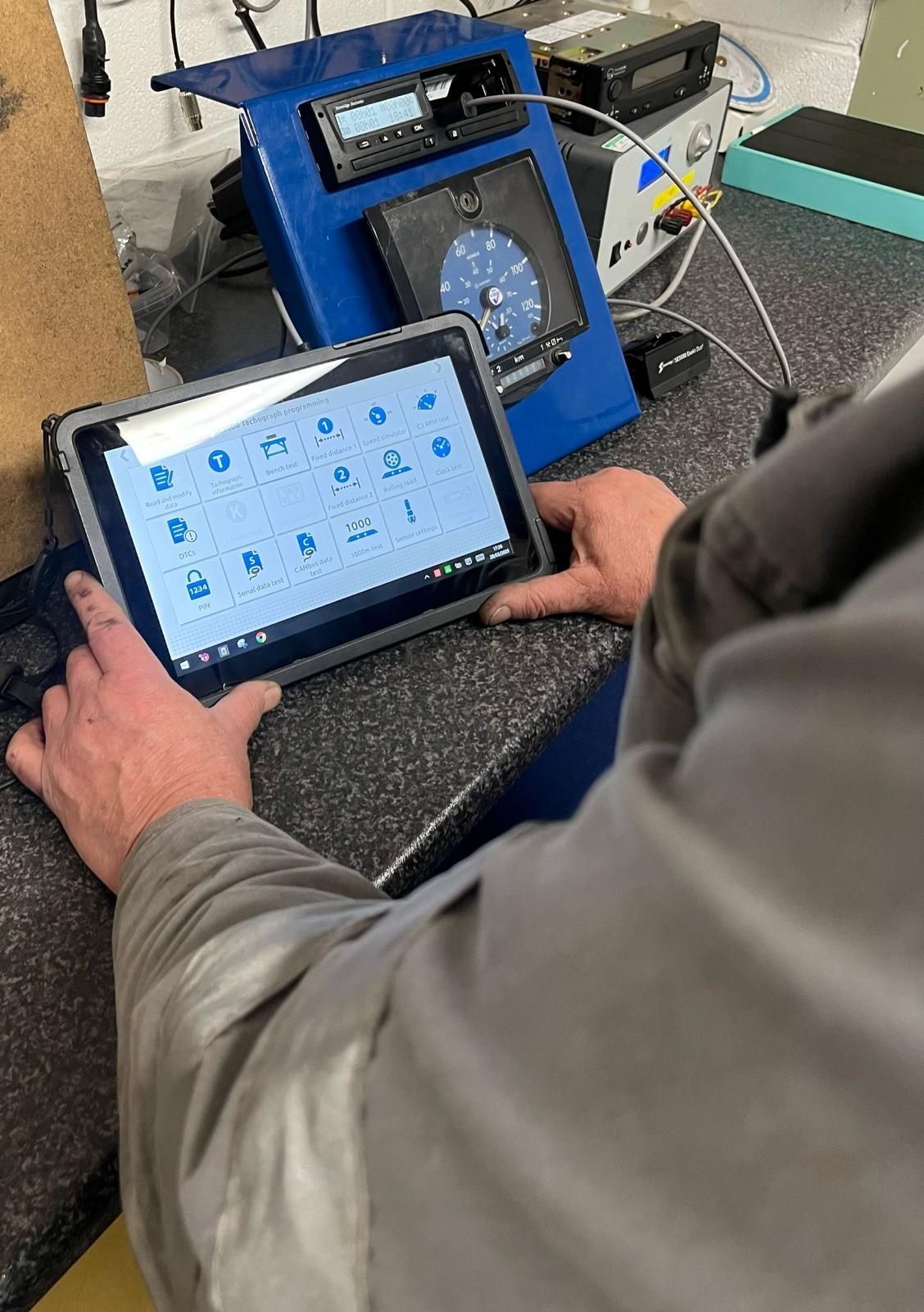 Person using a tablet beside a blue portable device in a workshop setting