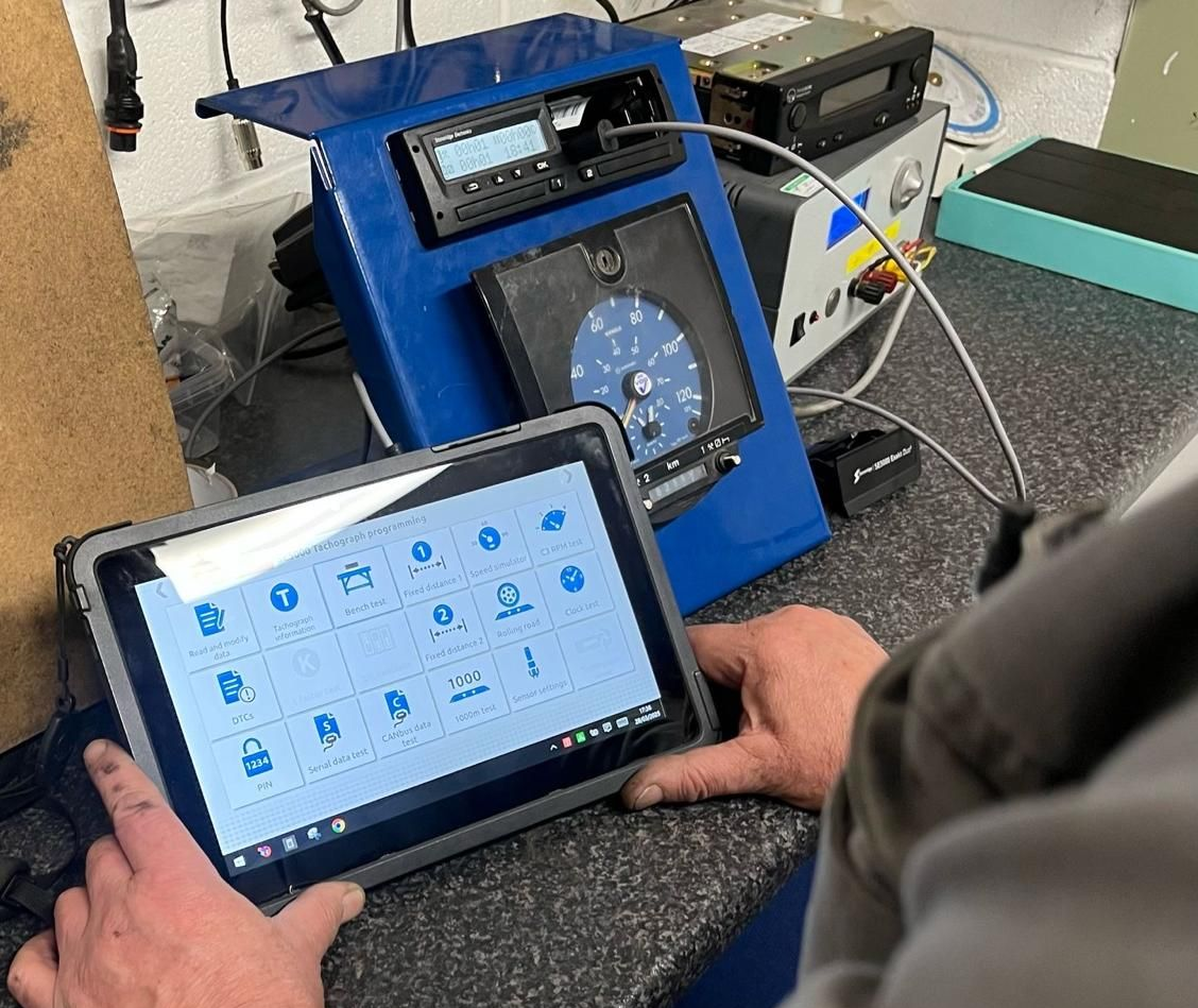 Hands holding a tablet in front of a blue control machine on a workbench.