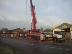 Red crane and white truck at a roadside construction site near houses and green buildings