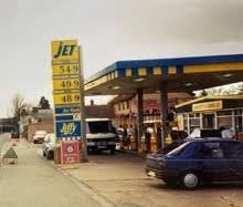 Gas station with a tall JET price sign, cars at the pumps, and a blue car in the foreground.