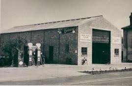 Vintage black-and-white photo of a brick gas station with fuel pumps and an open garage bay