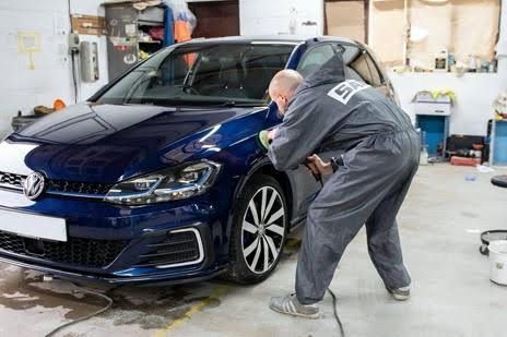 Mechanic polishing a dark blue car in an auto shop