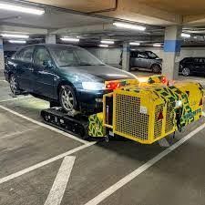 Dark sedan in parking garage with a yellow Manchetts industrial device mounted at the front.