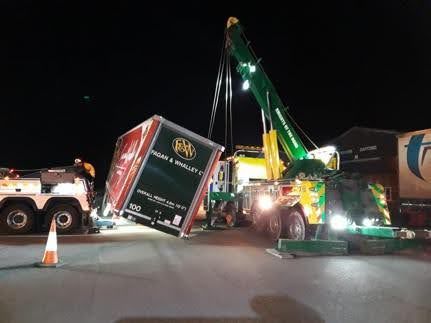 Manchetts Tow truck lifting a toppled trailer on a dark road at night with traffic cones nearby