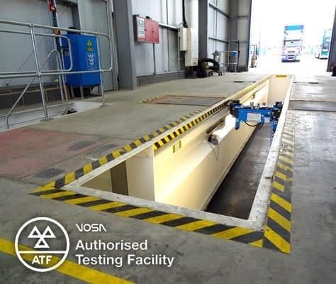 Industrial testing pit with yellow-black caution stripes and a blue machine in an indoor facility