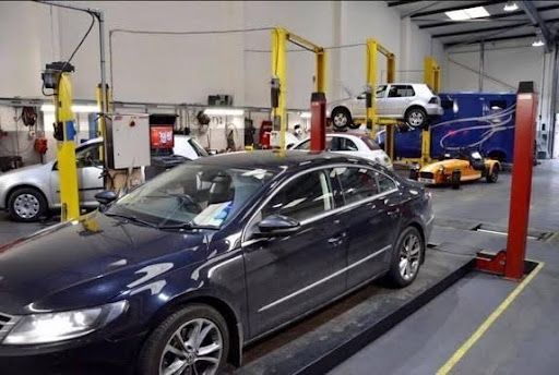 Cars in an auto repair shop with lifts and a mechanic working in the background