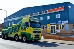 Yellow-and-green Manchetts Renault truck parked outside a blue truck dealership building